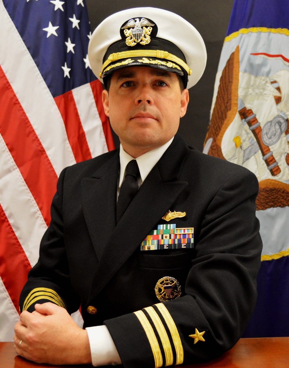 Commander Paul Chabot in U.S. Navy dress uniform in front of the American and Navy flags